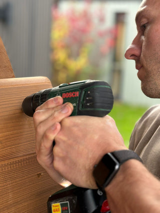 Immerse co-founder Dan building a wooden Finnish sauna holding a drill