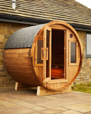 Wooden barrel-shaped sauna on a patio with a stone building in the background